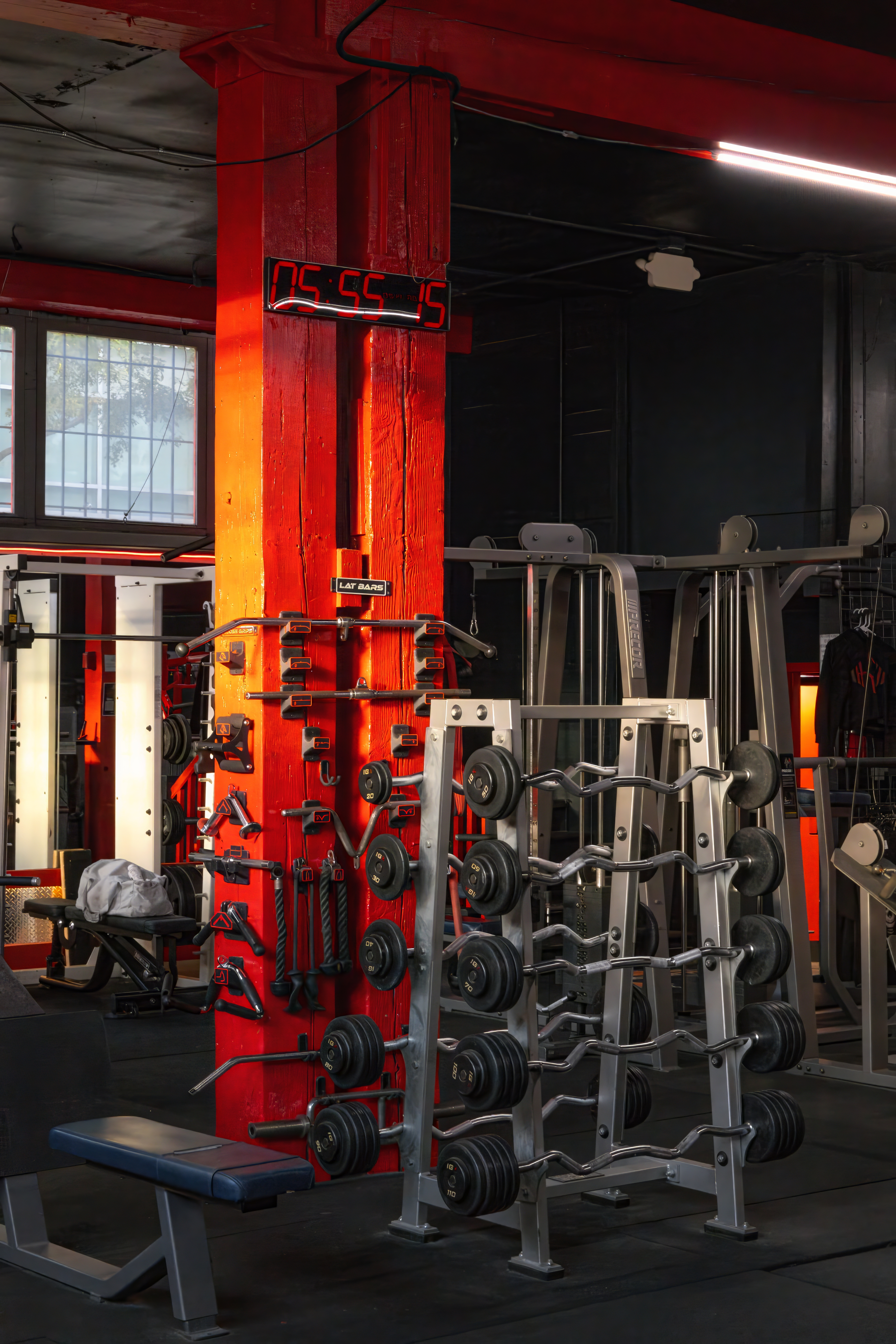 Barbell and accessory storage area featuring a wall rack for lat bars, ropes, and handles, next to a vertical rack for EZ curl bars and fixed weight barbells