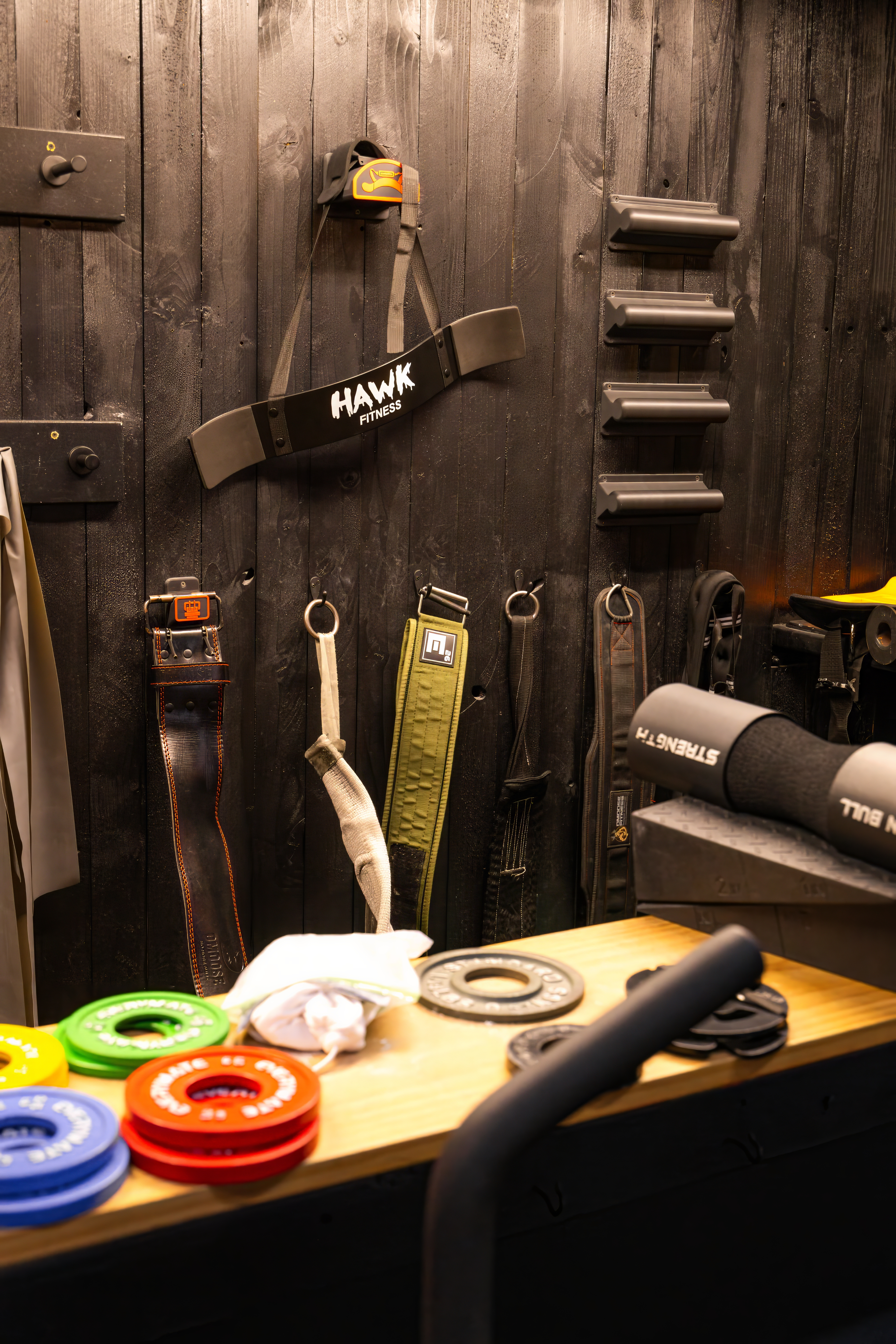 Dedicated storage wall for lifting accessories, including wrist wraps, Hawk Fitness arm blasters, belts, and competition fractional weight plates