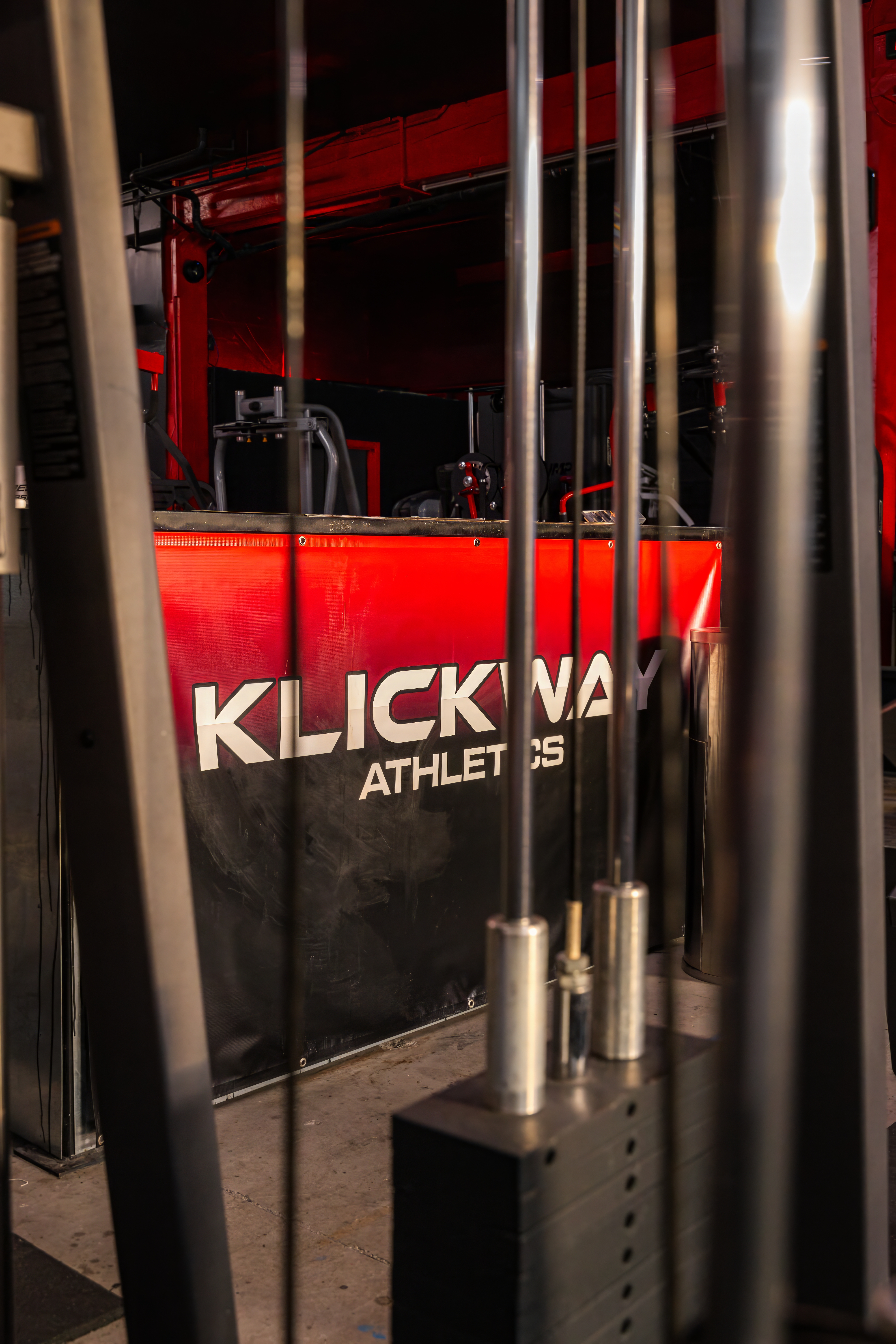 Detailed view of the KlickWay Athletics branding displayed on a gym banner, framed by the cables and weight stacks of a multi-station cable machine
