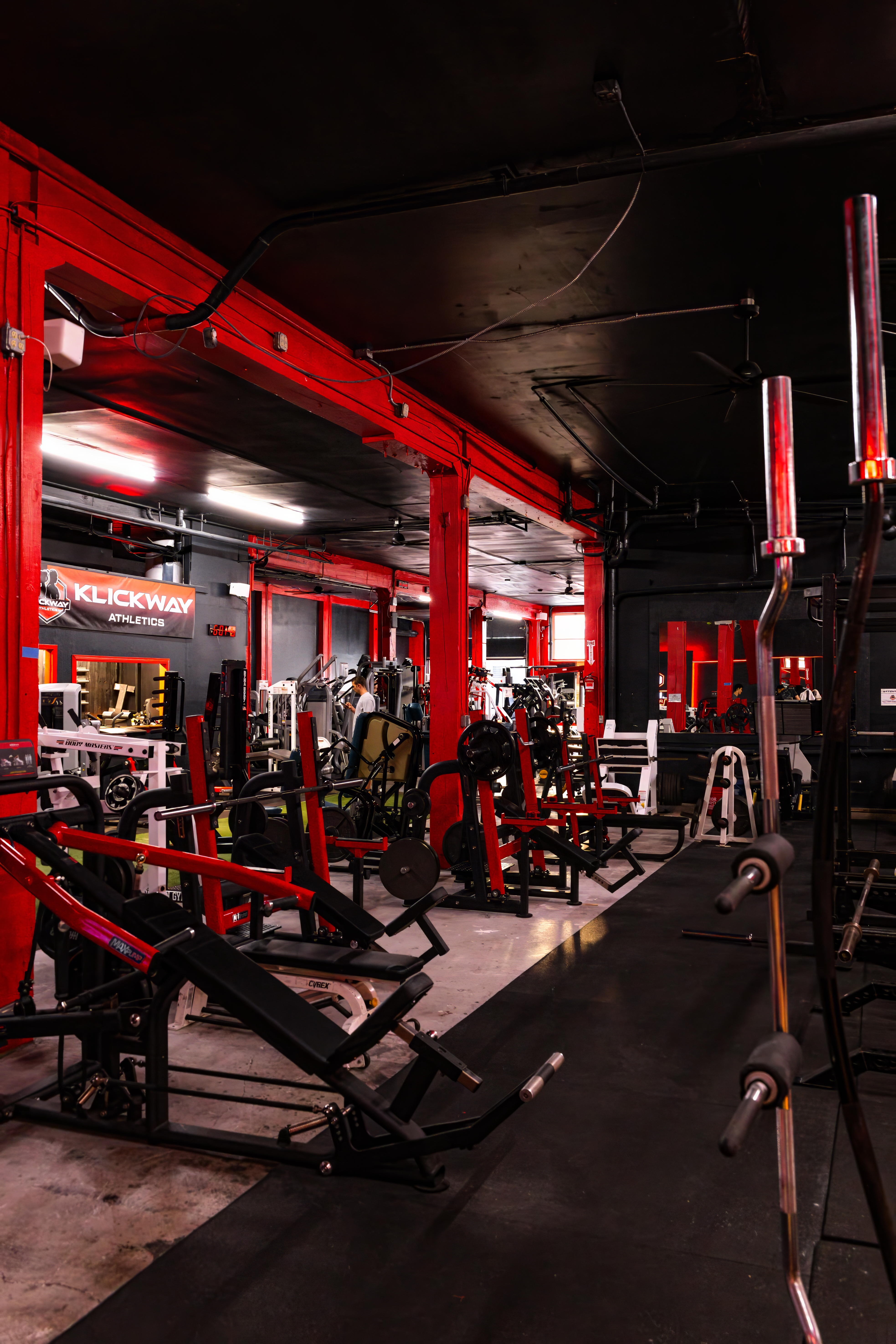 Wide, clear view down the main equipment aisle of KlickWay Athletics, emphasizing the long array of modern, heavy-duty strength machines