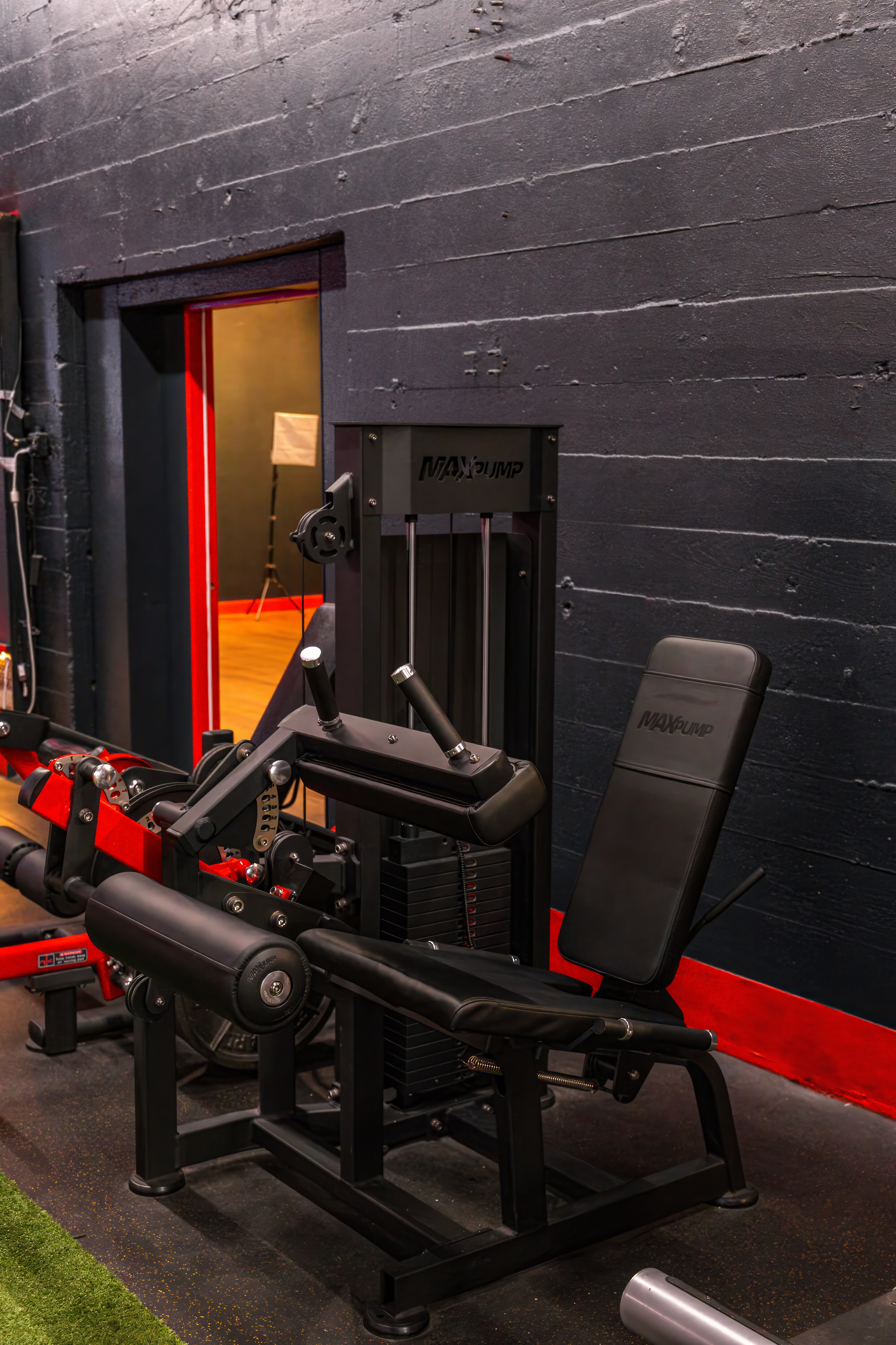 Maxum selectorized leg extension machine with a weight stack, set against the gym's dark, textured walls, offering a focused exercise for quad development