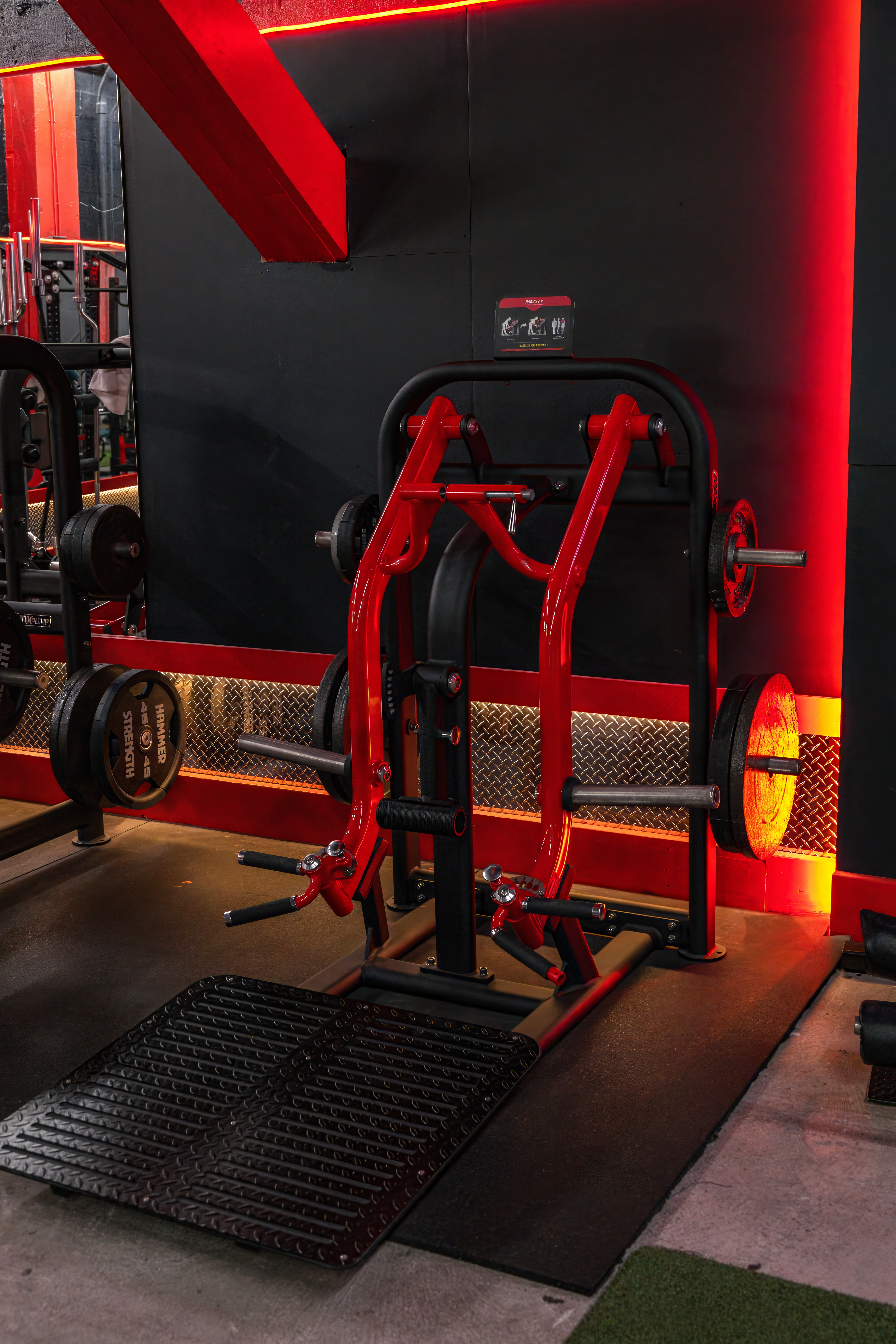 Specialized plate-loaded V-Squat machine with a vibrant red frame and large platform, a premium piece of equipment for deep and challenging lower-body workouts