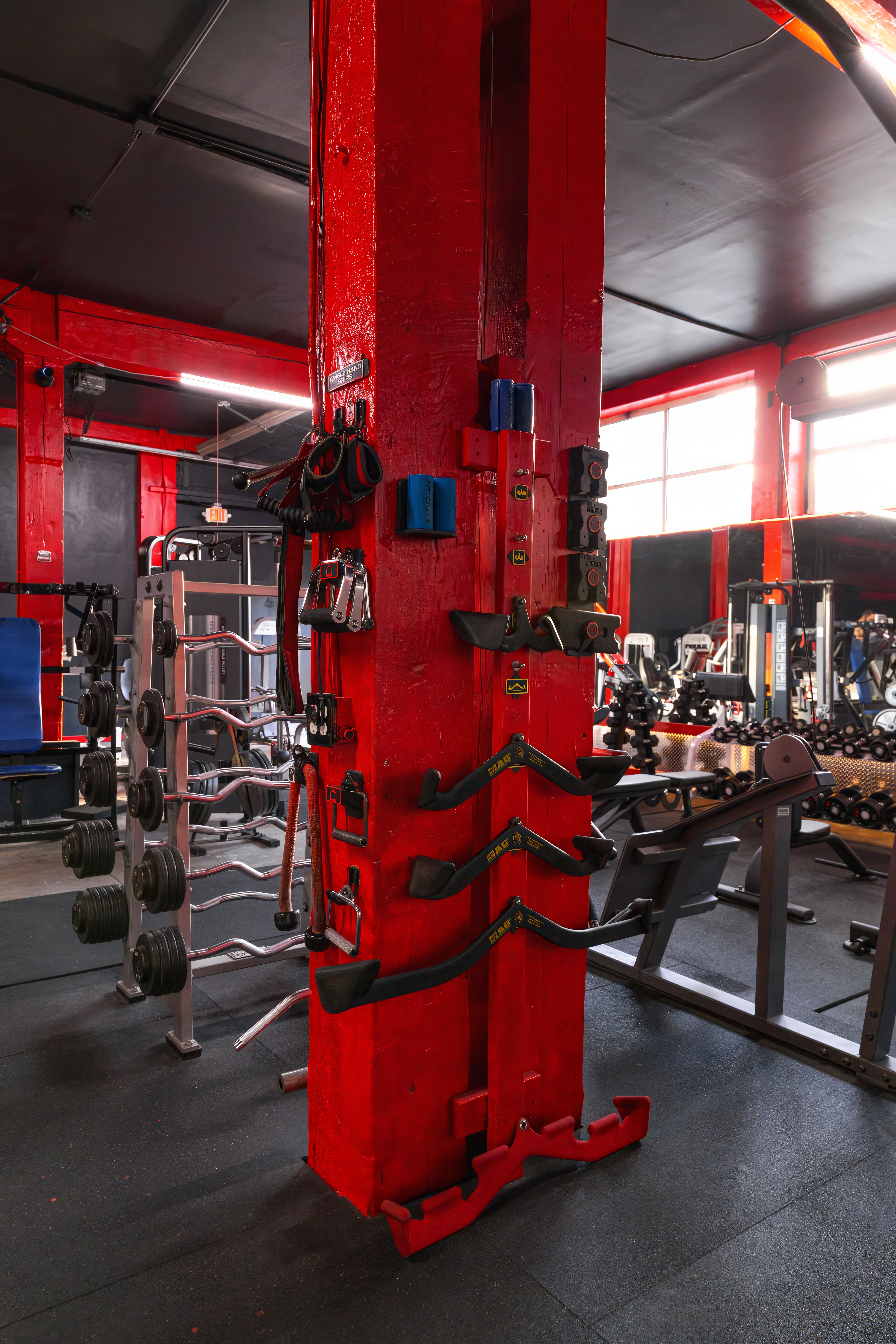 Central red pillar storage system for various lat pull-down bars, ropes, and specialized handles, conveniently located next to a rack of fixed barbells